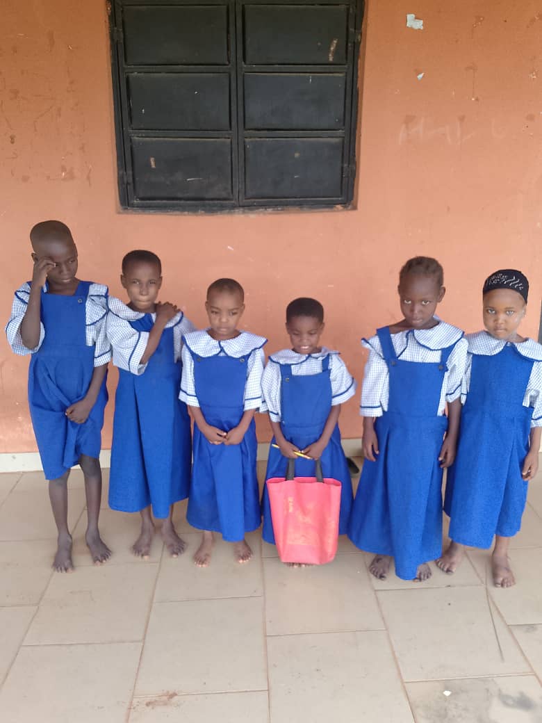Six children in blue school uniforms standing outside a classroom