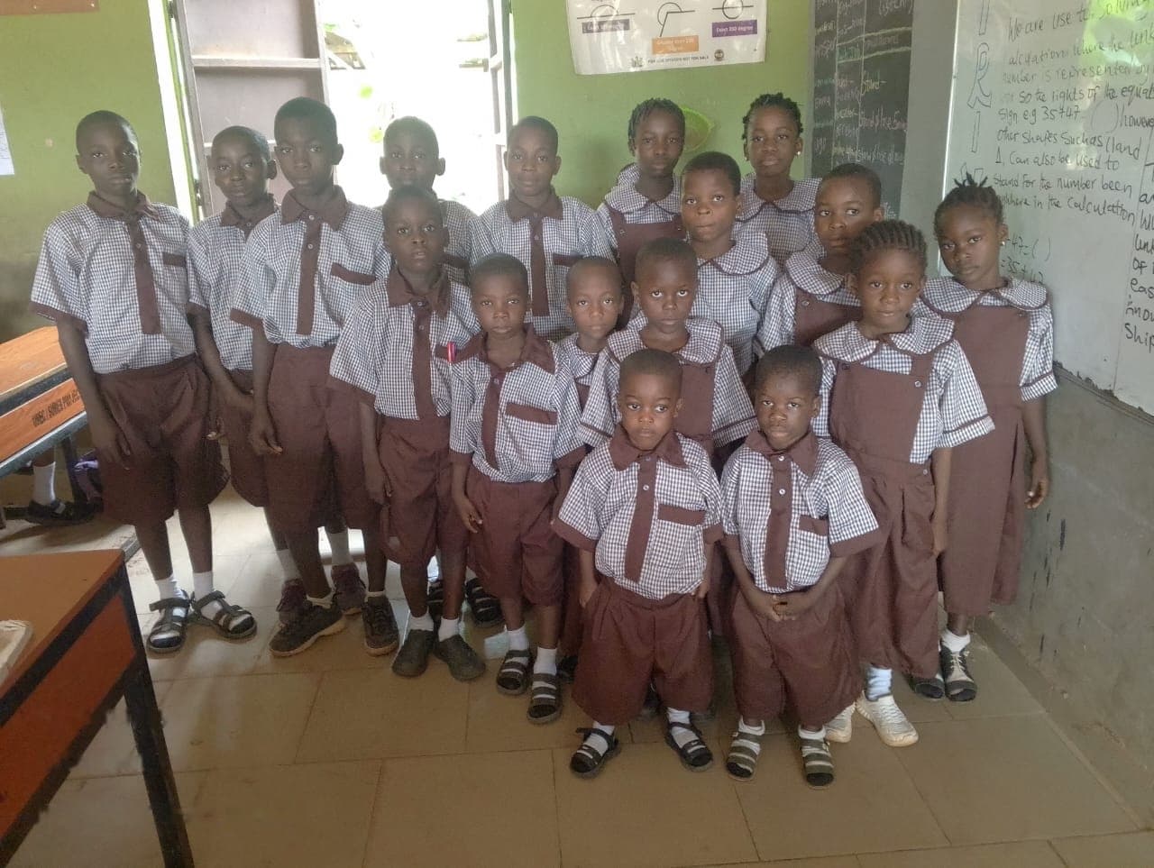 A group of pupils in brown and checked uniforms gathered in a classroom